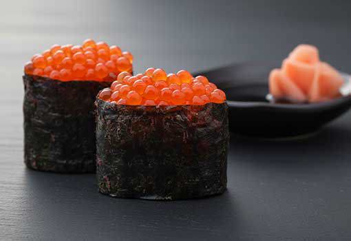 Two vibrant orange Priess & Co. trout caviar gunkan sushi pieces, wrapped in nori seaweed, with shiny reflections on a white surface." width="437"  height="300"